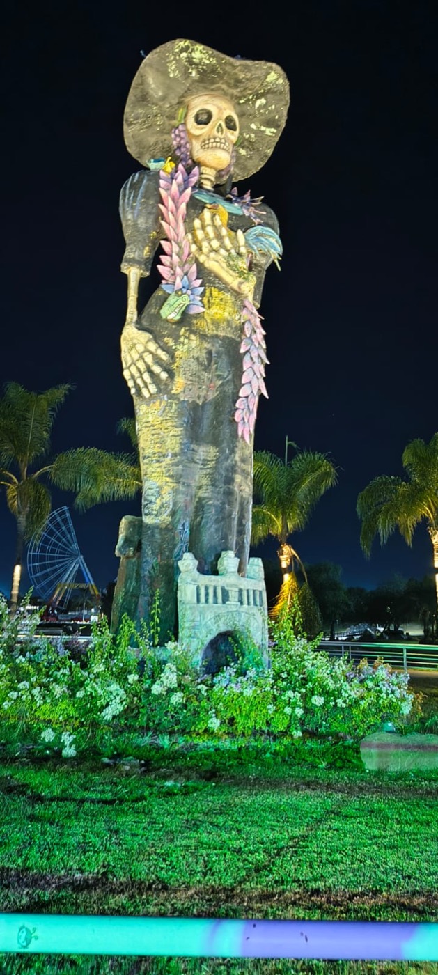 Catrina monumental de noche entre palmeras iluminadas